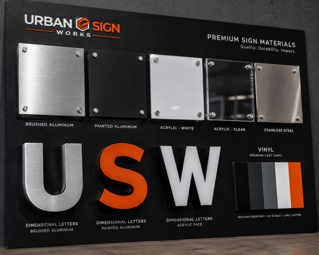 Close-up material board showing aluminum, acrylic, stainless steel and vinyl used in sign fabrication.