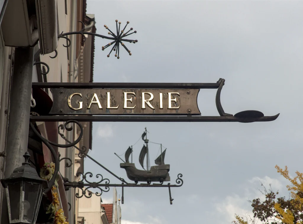 Photo of a double-sided illuminated blade sign projecting perpendicular from a boutique storefront over the sidewalk, showing how a projecting sign reaches pedestrians walking beneath it