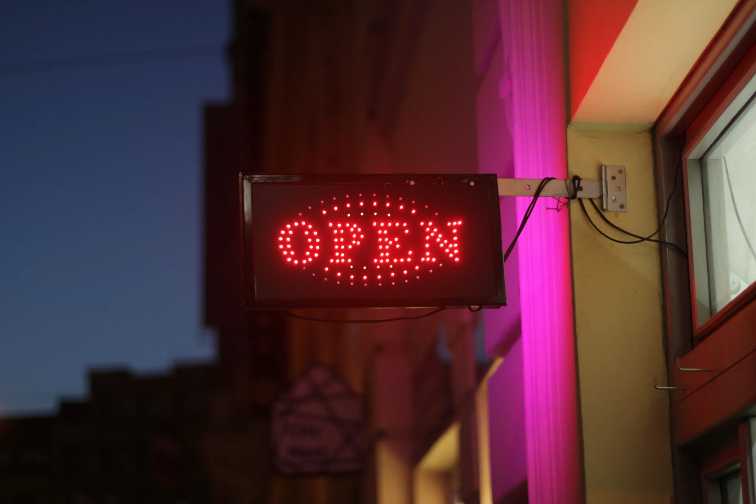 Warm red LED open sign glowing in a shop window at dusk