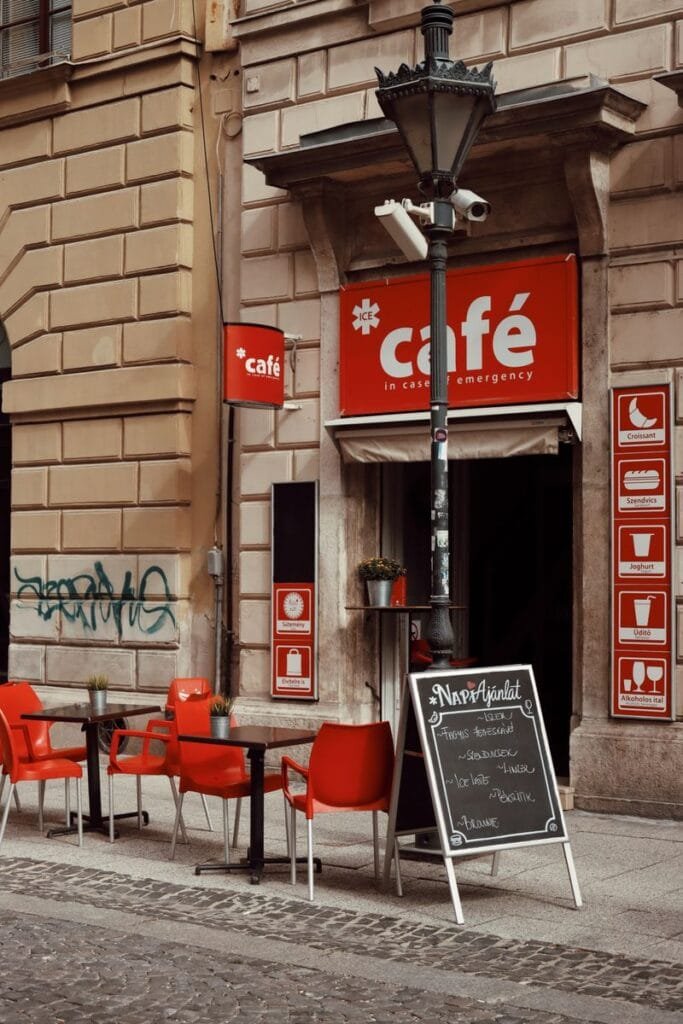 A-frame sign placed on the sidewalk outside a café storefront with a red awning, next to framed menu posters